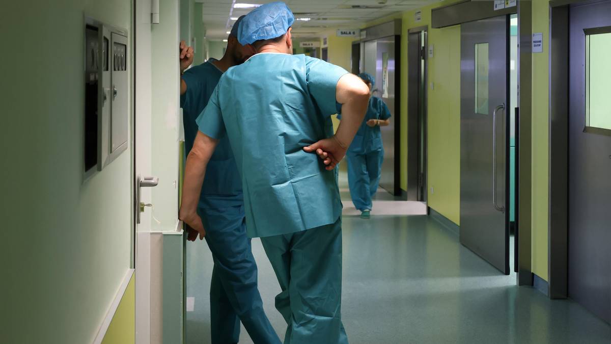 Korytarz szpitalny z personelem medycznym w turkusowych uniformach.