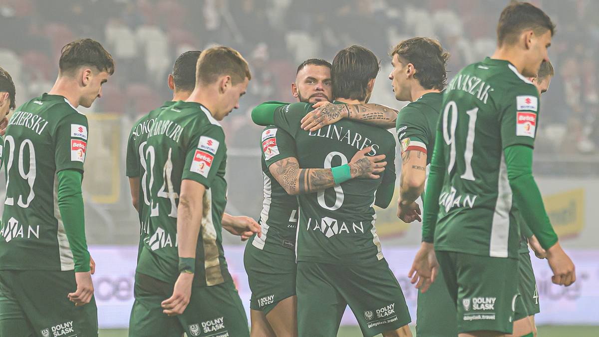 Piłkarze w zielonych strojach świętujący po zdobyciu bramki, przytulający się do siebie na boisku.