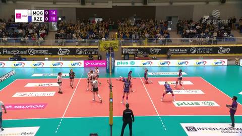 Mecz siatk&oacute;wki, zawodnicy na boisku, w tle trybuny z kibicami.