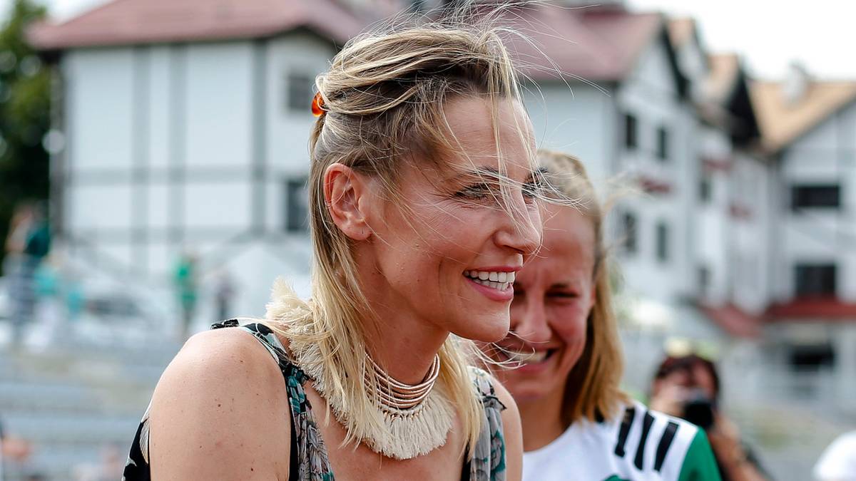 Sylwia Gruchała uśmiecha się, odbierając coś od drugiej kobiety.