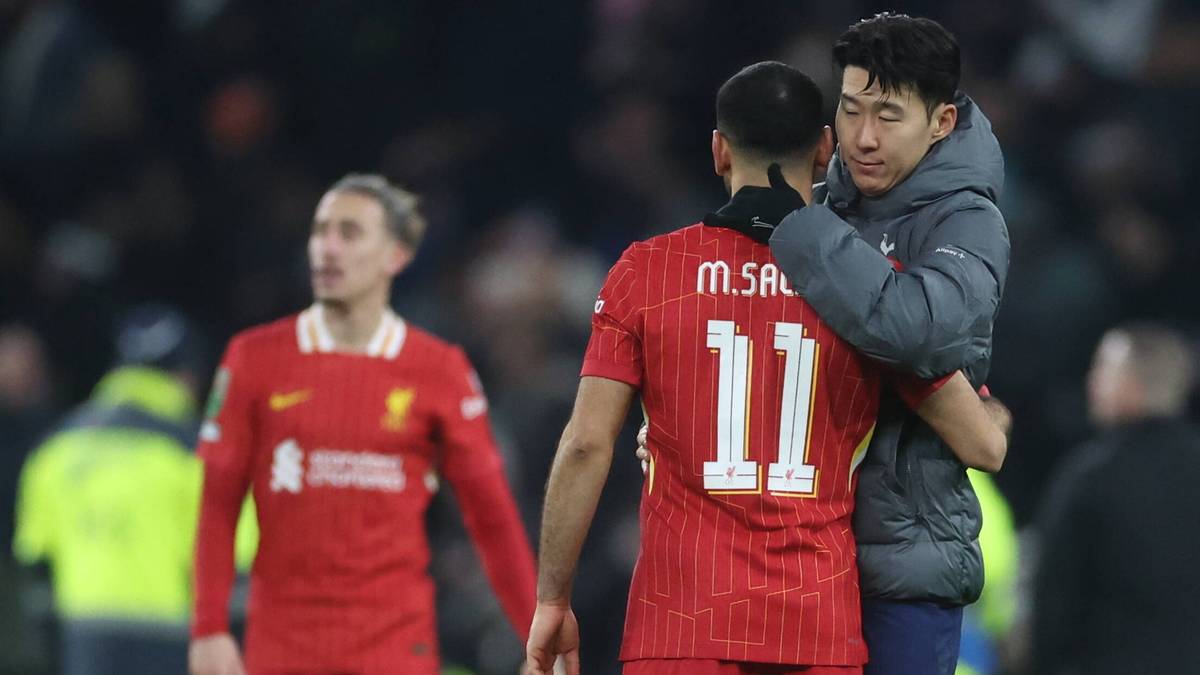 Dwóch piłkarzy przytulających się na boisku po meczu, jeden w czerwonej koszulce Liverpoolu, drugi w szarej kurtce z numerem 11 na plecach.