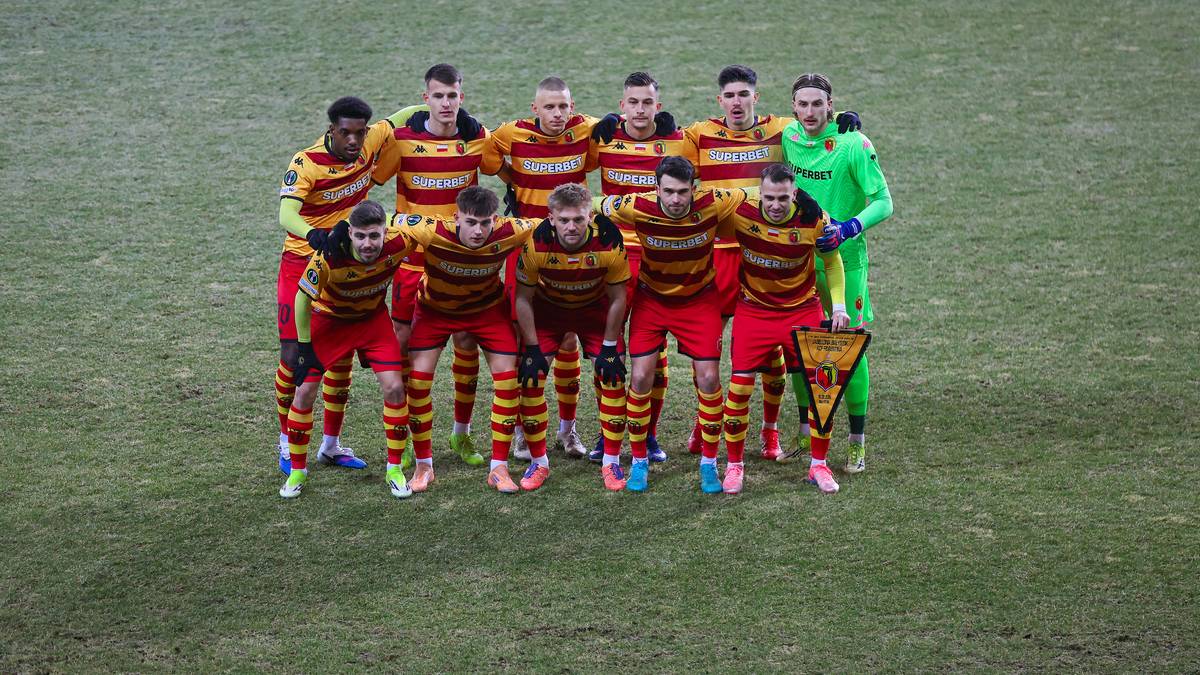 Drużyna piłkarska Jagiellonii Białystok pozująca do zdjęcia na boisku.