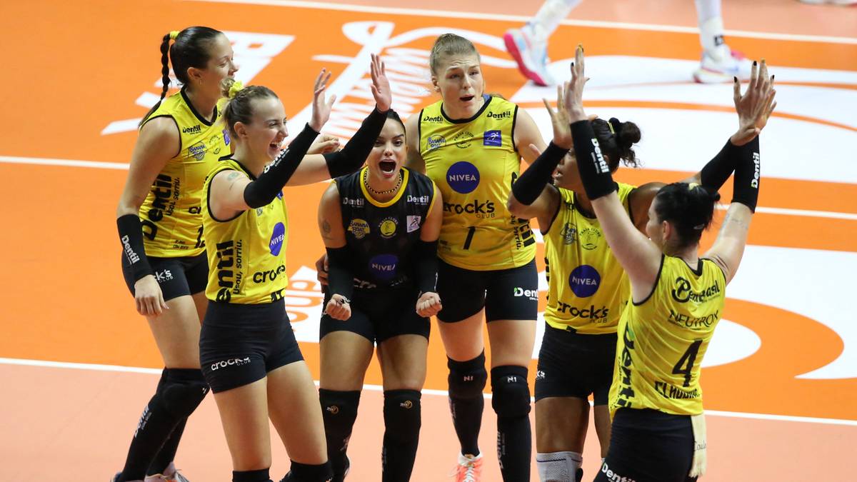 Siatkarki w żółto-czarnych strojach świętują zwycięstwo, podnosząc ręce w górę.