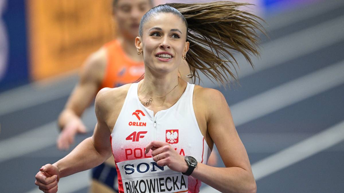 Lekkoatletka w białej koszulce z czerwonymi elementami biegnie po bieżni.