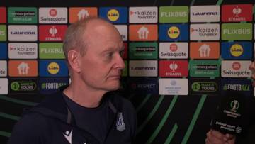 Portret Nielsa Frederiksena, trenera, z poważnym wyrazem twarzy, na tle paneli reklamowych.