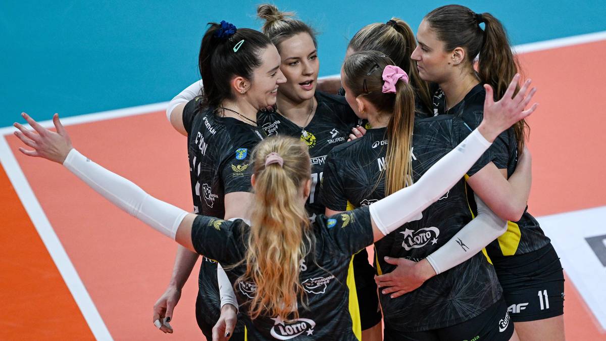 Grupa siatkarek w czarnych strojach cieszy się wsp&oacute;lnie na boisku.