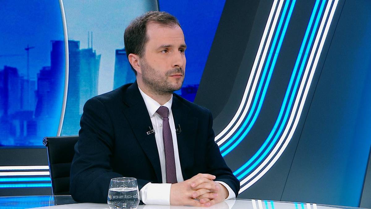 Mężczyzna w garniturze siedzi przy stole w studiu telewizyjnym.