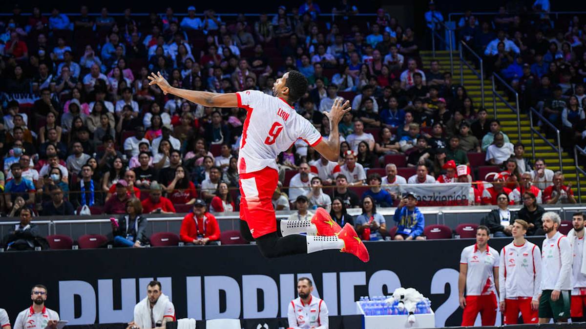 Siatkarz w skoku podczas meczu, w białej koszulce z czerwonym numerem 9 na plecach.