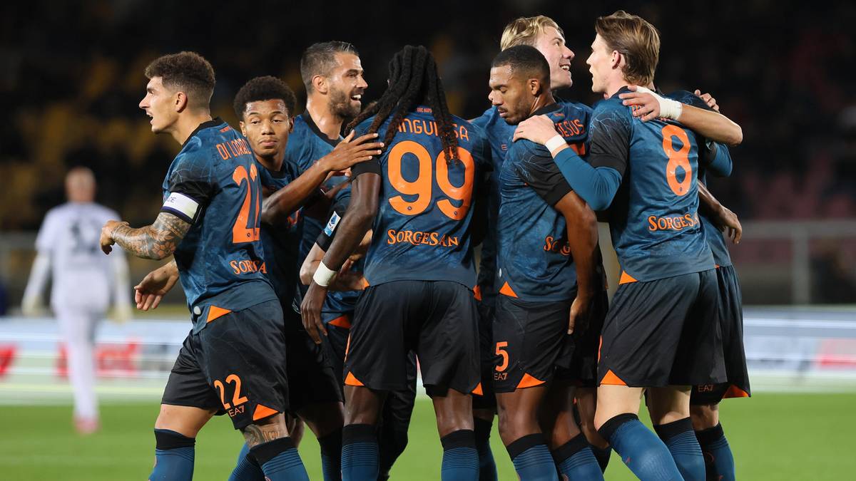 Drużyna piłkarska Napoli w niebiesko-pomarańczowych strojach świętuje zwycięstwo na boisku, obejmując się nawzajem.