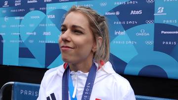 Aleksandra Mirosław w bluzie z medalem na szyi, na tle baneru z logo Igrzysk Olimpijskich Paryż 2024