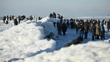 Ludzie obserwują lodowe formacje na zamarzniętym wybrzeżu podczas mroźnego dnia.