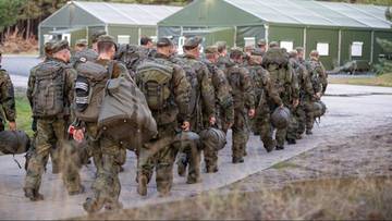 Żołnierze Bundeswehry w pełnym oporządzeniu idący w kierunku budynk&oacute;w wojskowych.