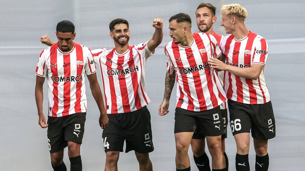 Pięciu piłkarzy w białych koszulkach w pionowe czerwone pasy i czarnych spodenkach świętuje radośnie po zdobyciu bramki.