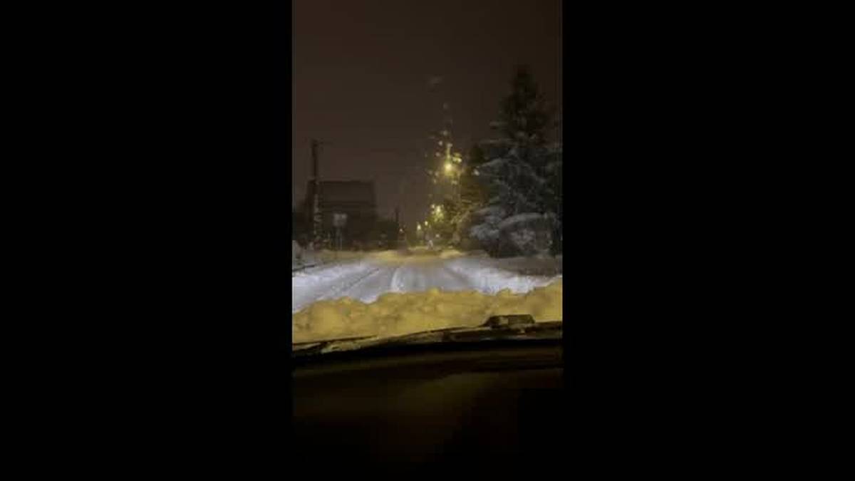 Droga w Słupsku pokryta grubą warstwą śniegu, widoczne drzewa obsypane białym puchem i latarnie uliczne oświetlające nocną scenę.