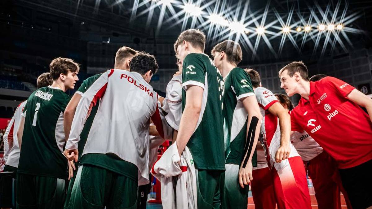 Grupa siatkarzy w strojach sportowych zebrana w kręgu, rozmawiająca w trakcie meczu.