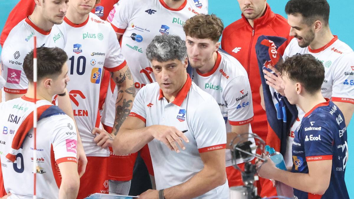 Trener siatk&oacute;wki omawia taktykę z zawodnikami w białych strojach sportowych.