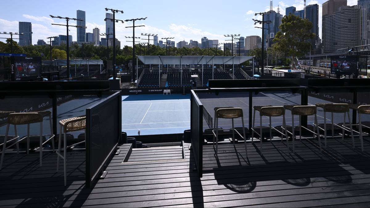 Widok na kort tenisowy z zacienionego miejsca z krzesłami w pierwszoplanowym planie i panoramą miasta w tle.