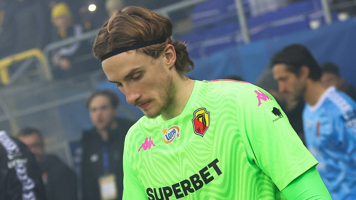 Bramkarz Jagiellonii Białystok w zielonej koszulce z numerem 50 wchodzi na boisko, obok niego idzie młody chłopiec w niebieskiej czapce.