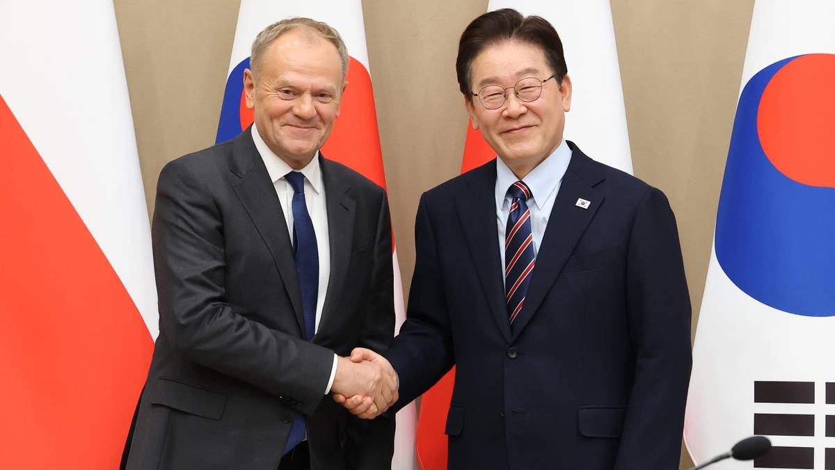 Dw&oacute;ch mężczyzn w garniturach ściska sobie dłonie na tle flag Polski i Korei Południowej.
