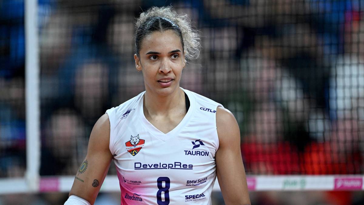 Siatkarka w białej koszulce z numerem 8, ze spiętymi włosami, z lekko zmęczonym wyrazem twarzy, na tle trybun.