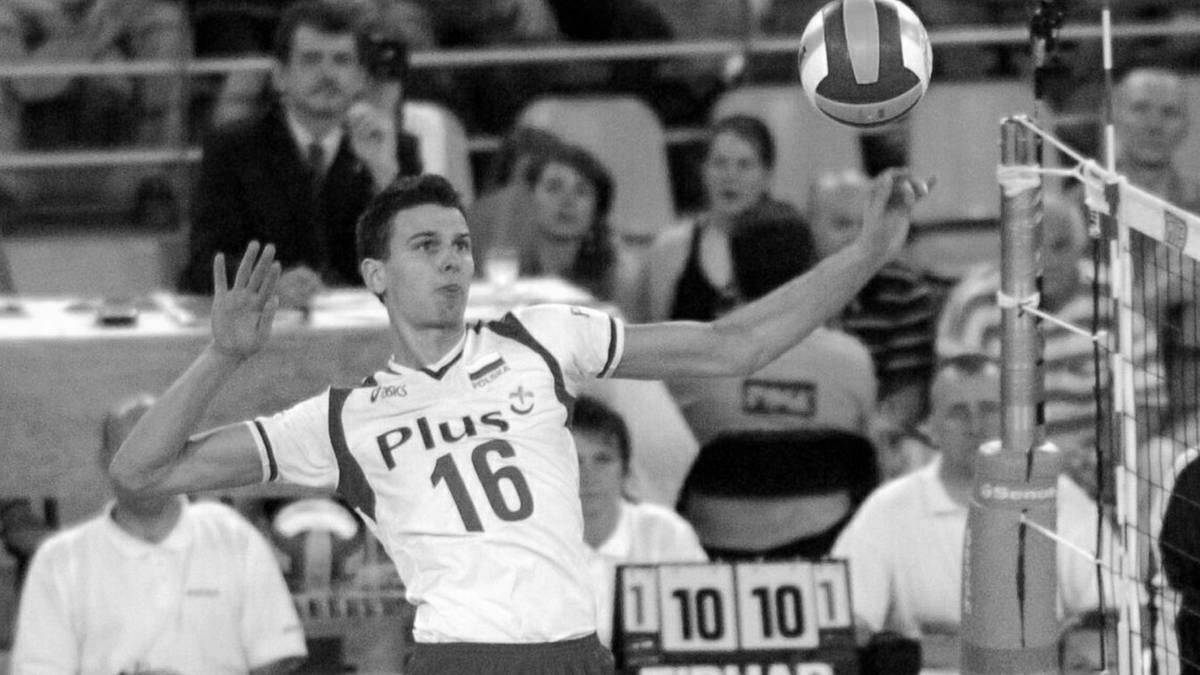 Siatkarz w białej koszulce z numerem 16 i napisem "Plus", wykonuje zagrywkę, piłka leci w powietrzu.