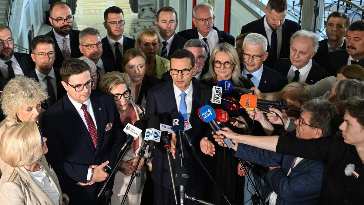Grupa polityków, w tym Mateusz Morawiecki, otoczona przez dziennikarzy z mikrofonami.