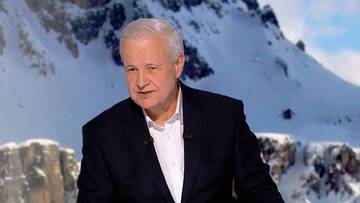 Starszy mężczyzna w białej koszuli i czarnej marynarce na tle zaśnieżonych g&oacute;r.