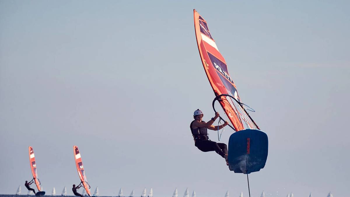 Żeglarz na desce windsurfingowej z kolorowym żaglem w akcji.
