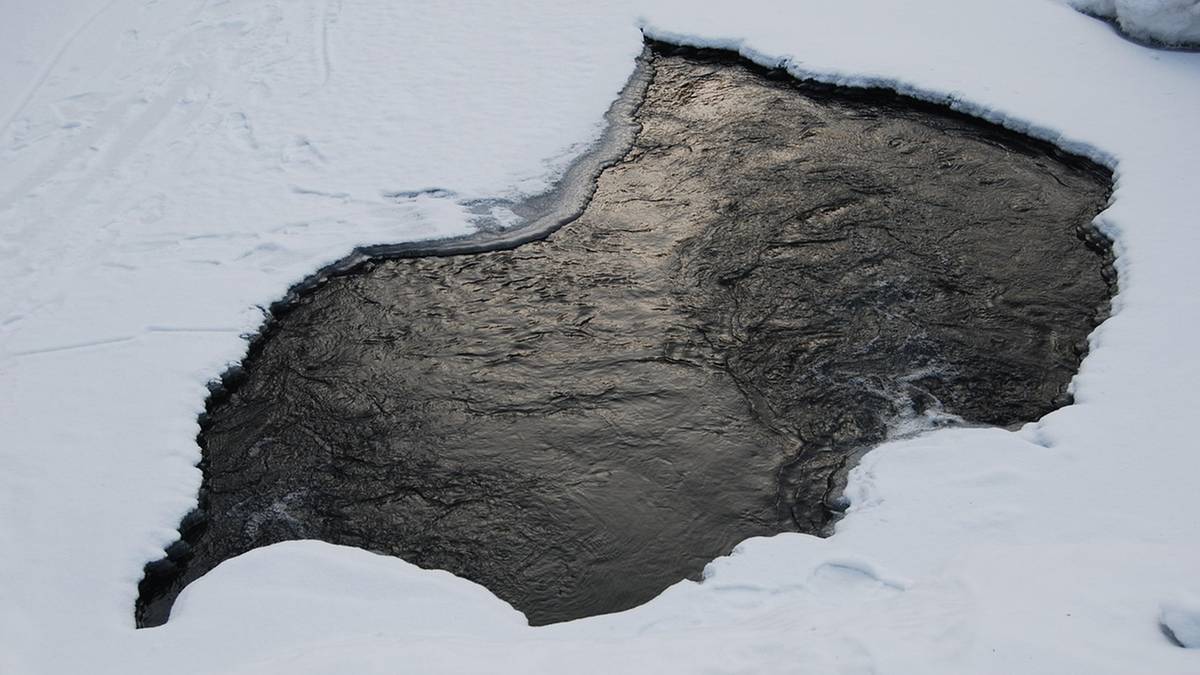 Przerębel w lodzie na zamarzniętym stawie, z widoczną ciemną wodą wewnątrz.