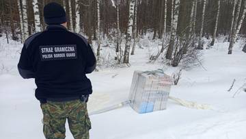 Funkcjonariusz Straży Granicznej w zimowym lesie przy paczce papieros&oacute;w, kt&oacute;ra została dostarczona za pomocą balonu.