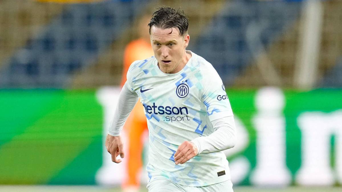 Piłkarz w białej koszulce z numerem 7 prowadzi piłkę na murawie stadionu.