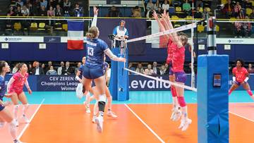 Siatkarki w akcji podczas meczu Ligi Mistrzyń, jedna próbuje zablokować atak przeciwniczki nad siatką.