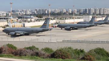 Samoloty wojskowe zaparkowane na płycie lotniska przed miejską zabudową.