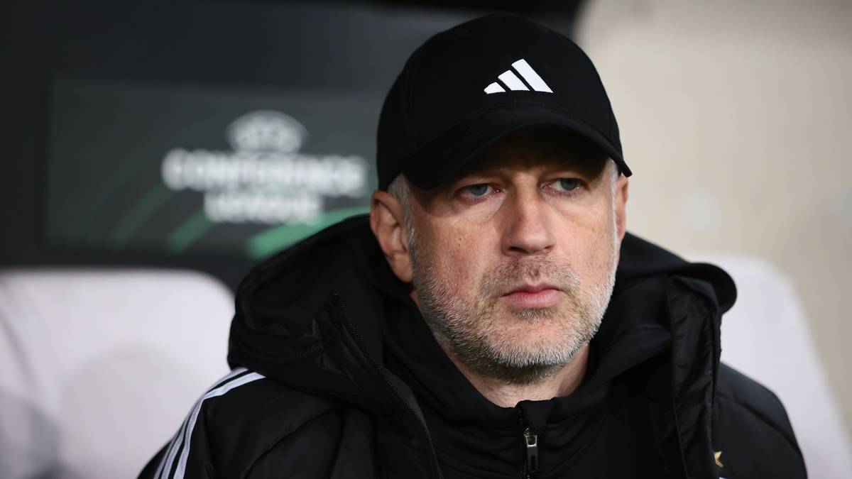 Mężczyzna w czapce z daszkiem z logo Adidas, ubrany w kurtkę z tym samym logo, siedzi i patrzy przed siebie z zamyślonym wyrazem twarzy.