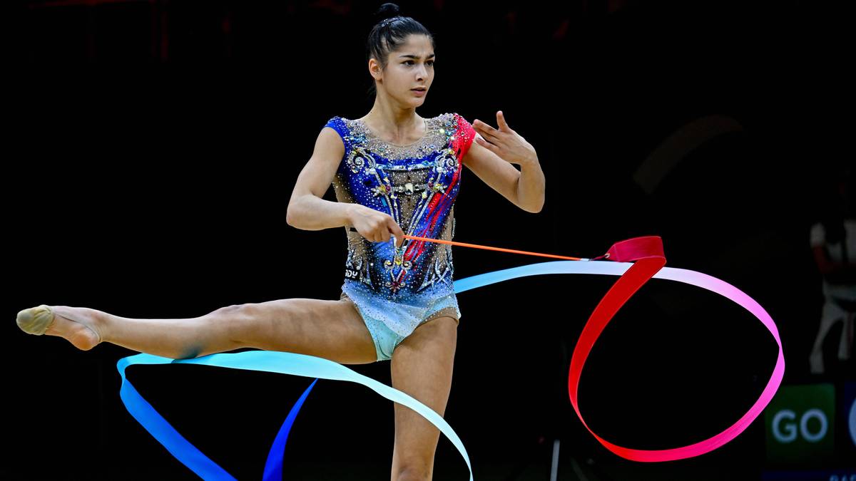 Sportsmenka wykonuje układ gimnastyki rytmicznej z taśmą w kolorze niebieskim i czerwonym.