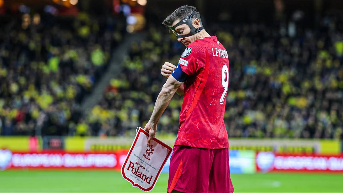 Piłkarz reprezentacji Polski w masce ochronnej trzyma tabliczkę z napisem "Poland".