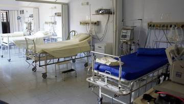 Widok wnętrza sali szpitalnej z kilkoma ł&oacute;żkami medycznymi na k&oacute;łkach i sprzętem monitorującym.