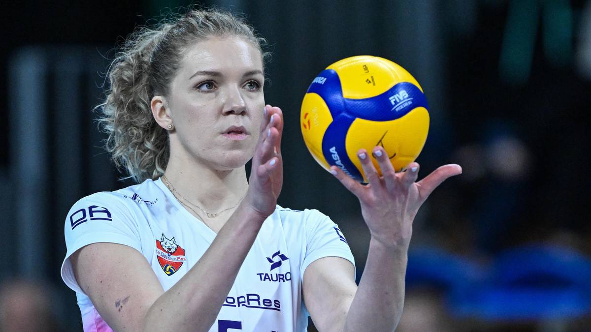 Siatkarka w białej koszulce z numerem i emblematem drużyny, trzymająca żółto-niebieską piłkę siatkową w dłoniach przed serwowaniem.