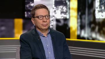 Mężczyzna w okularach siedzi i patrzy przed siebie.