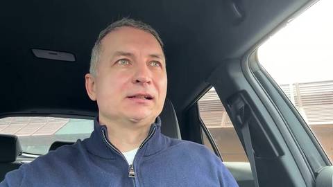 Portret mężczyzny w granatowej bluzie siedzącego w samochodzie.