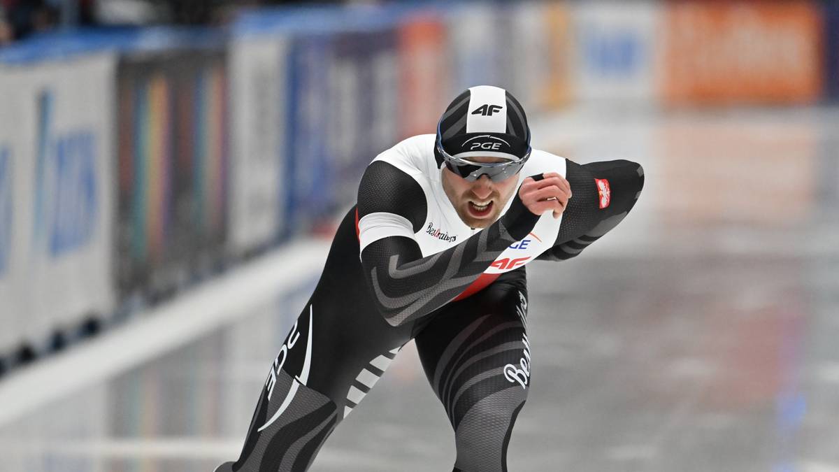 Łyżwiarz szybki w czarno-białym kombinezonie na lodowym torze.