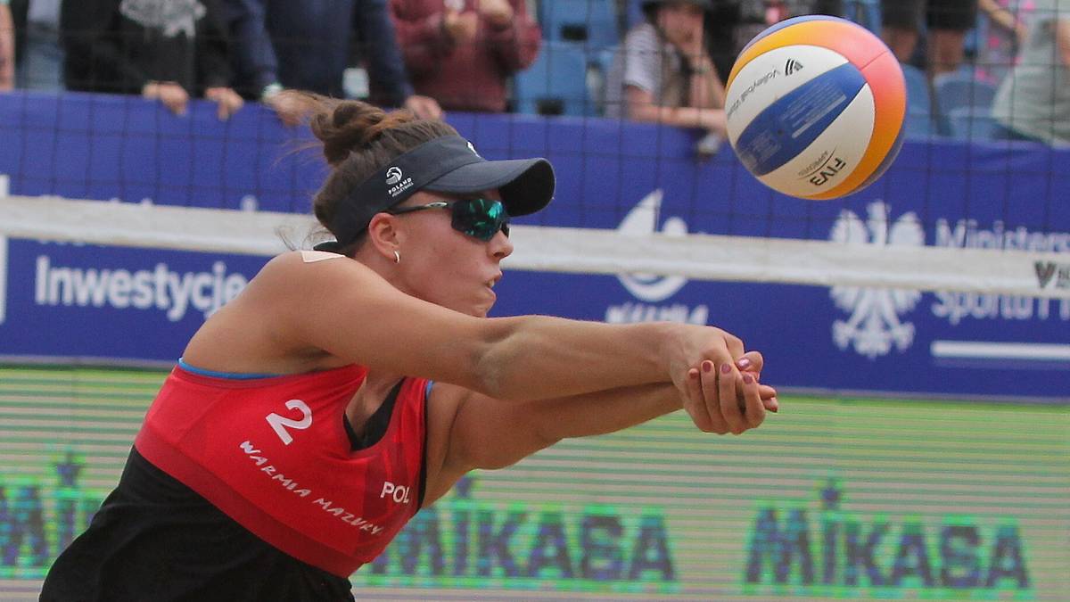 Siatkarka plażowa z Polski w czerwonym stroju i okularach przeciwsłonecznych odbija piłkę.