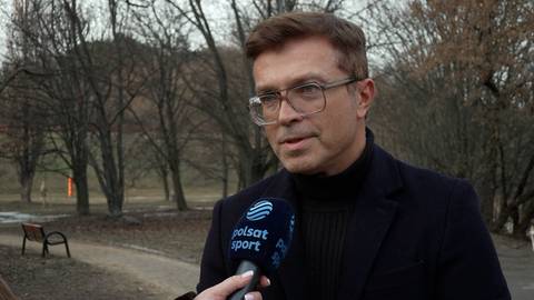 Bożydar Iwanow w okularach i czarnym golfie udziela wywiadu, trzymając mikrofon Polsat Sport. W tle park z drzewami i ławką.