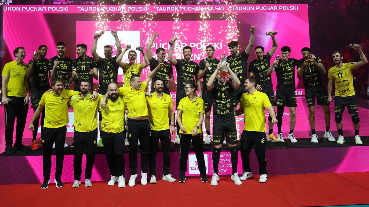 Drużyna siatkarska Bogdanka LUK Lublin w ż&oacute;łto-czarnych strojach, pozująca do zdjęcia na podium, otoczona konfetti i fajerwerkami.