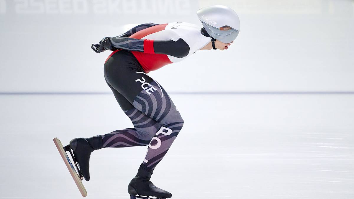 Zawodniczka w kombinezonie do łyżwiarstwa szybkiego na lodzie, pochylona do przodu z łyżwą na nodze.