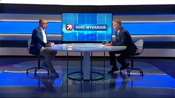 Dw&oacute;ch mężczyzn siedzi przy okrągłym stole w studiu telewizyjnym.