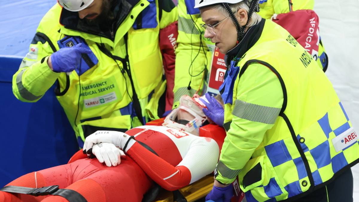 Zawodniczka short tracku na noszach, otoczona przez ratownik&oacute;w medycznych.