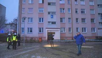 Funkcjonariusze policji i straży pożarnej przy wielopiętrowym bloku mieszkalnym, teren zabezpieczony taśmą.