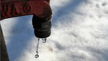 Czerwony metalowy zaw&oacute;r z kapiącą wodą na tle śniegu.