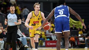 Dw&oacute;ch zawodnik&oacute;w podczas meczu koszyk&oacute;wki, jeden z nich trzyma piłkę.